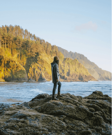 Man standing on a rocky shoreline, looking at the ocean