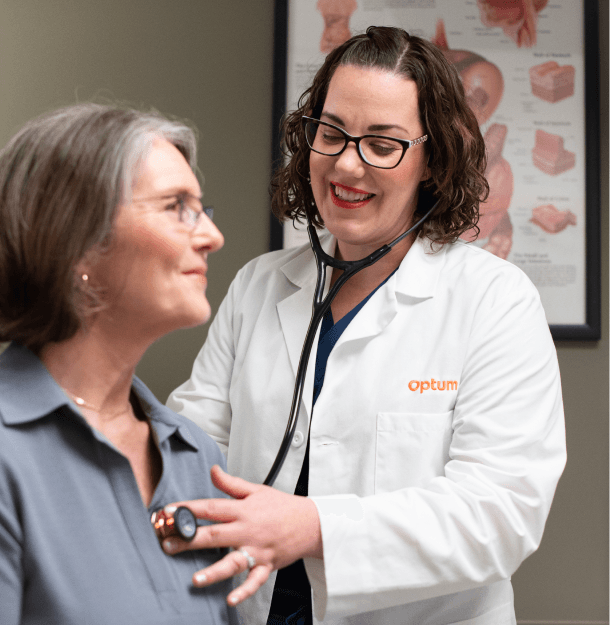 Optum OR doctor using a stethoscope to check a smiling female patient’s heart