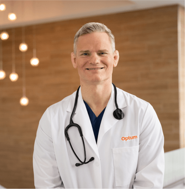 Smiling male doctor in an Optum white coat with a stethoscope