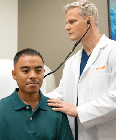 Optum OR doctor in a white coat using a stethoscope to examine a male patient